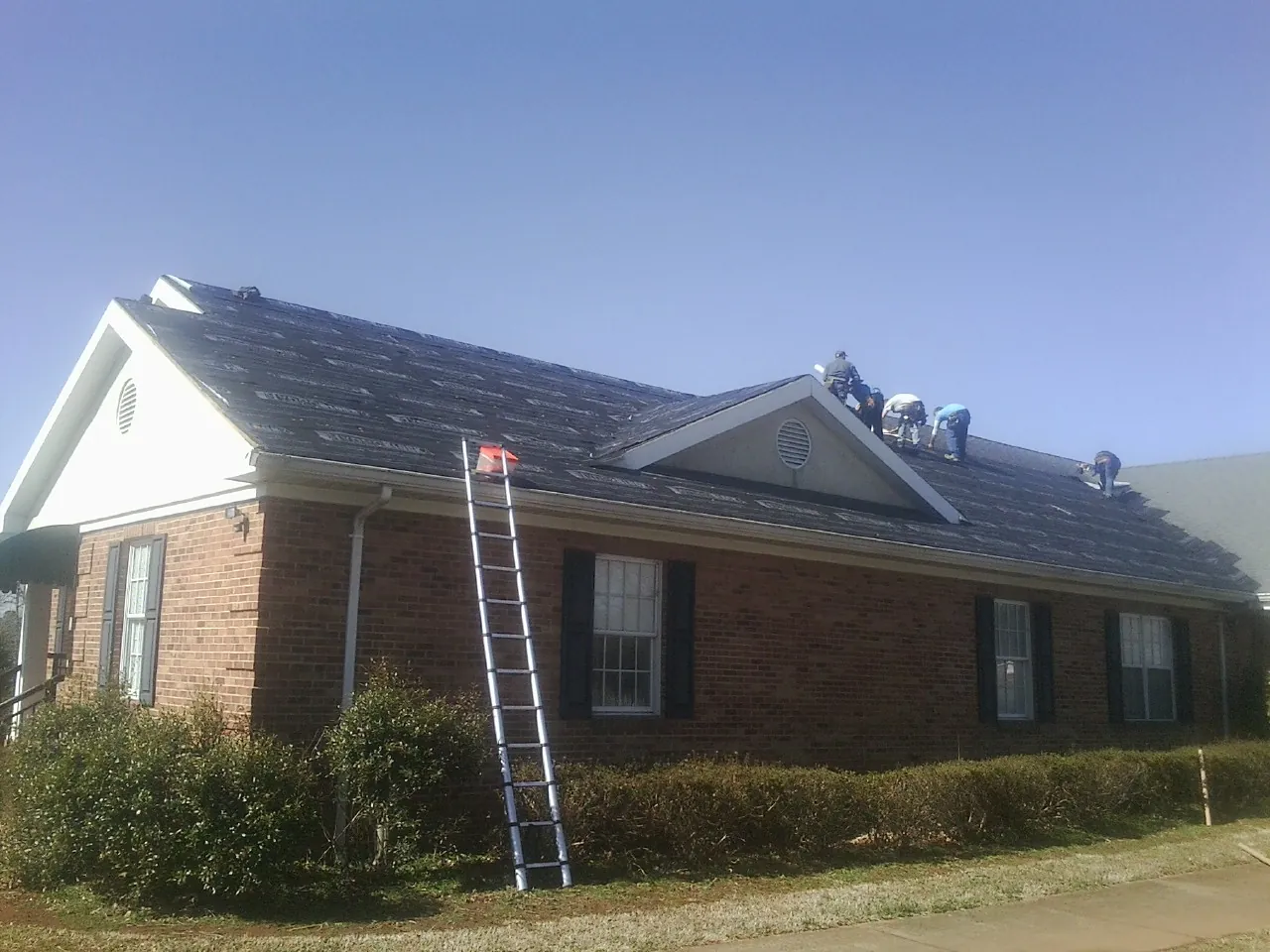 Crew tearing shingles off a brick ranch roof with a ladder set — Metal Roof Repair work by our crew in Calumet City