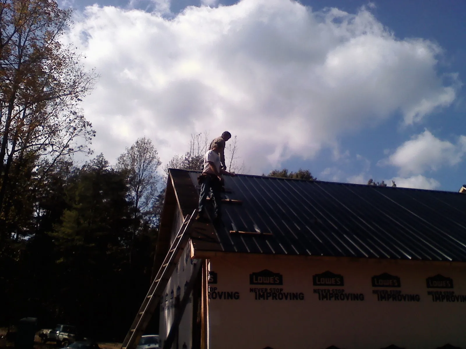 Roofer fastening dark metal panels high against a cloudy sky, from a Roof Inspection job in Calumet City