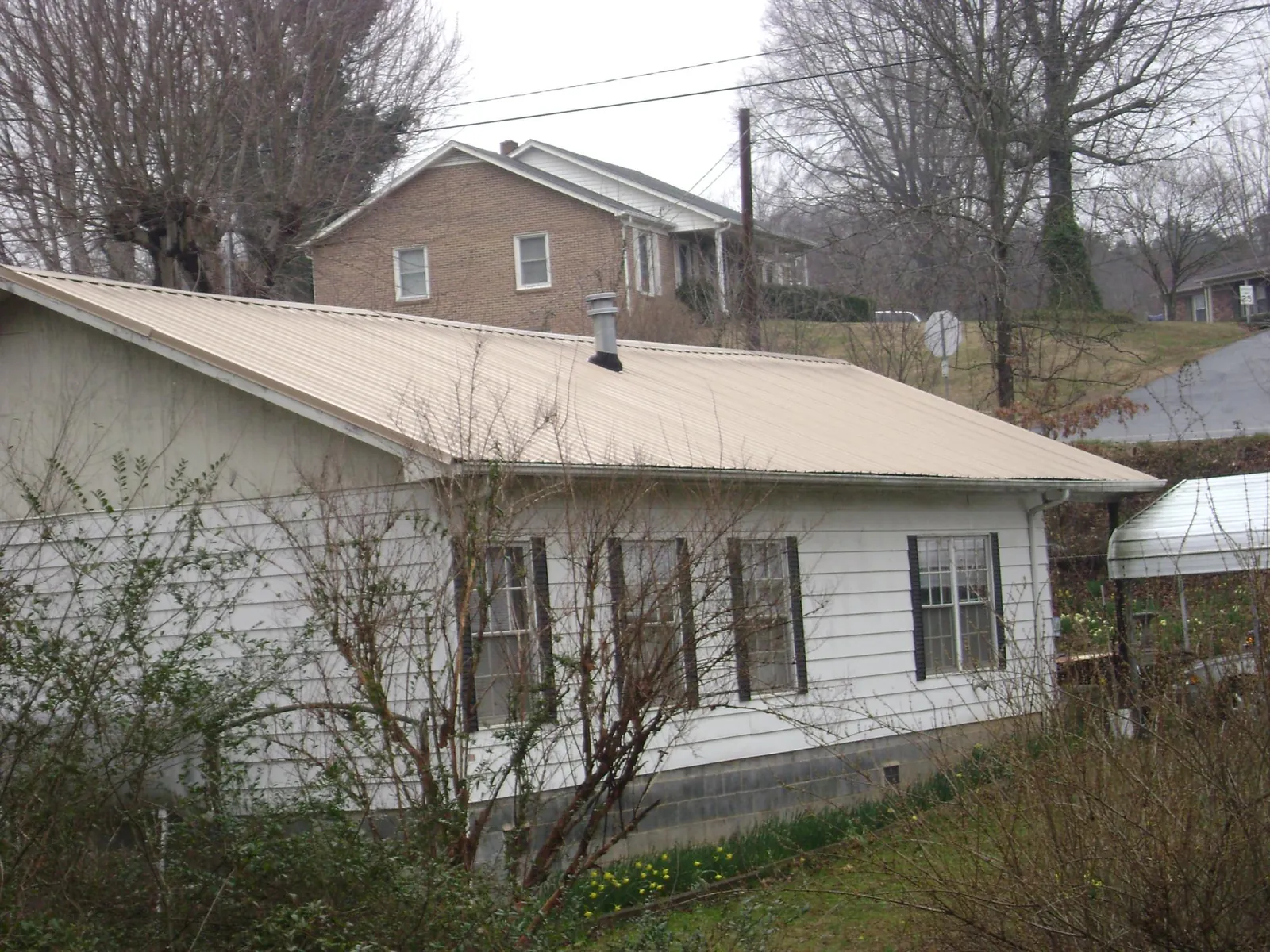 Tan metal roof on a white sided house set into a hillside — Commercial Roofing by Roofing Brothers in Calumet City